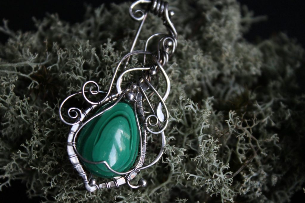 A detailed silver pendant with a green malachite stone.